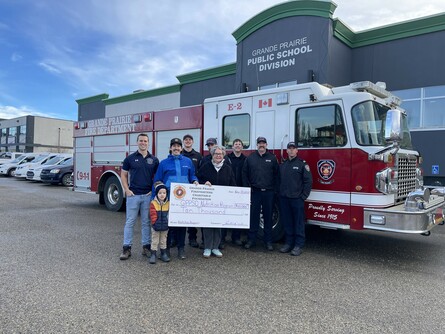 People standing in front of a firetruck with a giant cheque